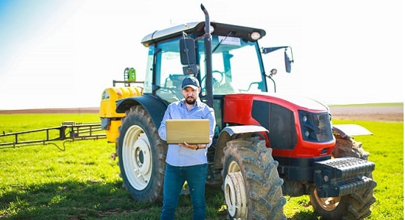 Man standing beside tractor with a laptop